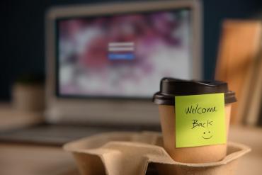 Photo of paper coffee cup with welcome back sticky note